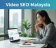 A Malaysian strategist reviews video results on a laptop in a bright office.