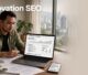 Man seated at a desk reviewing SEO analytics on a laptop, city skyline visible through a window behind him, with 'Renovation SEO' overlayed text.
